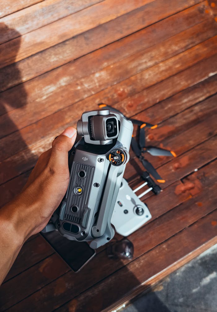 gallery-6 A close-up of a hand holding a drone against a wooden background outdoors.