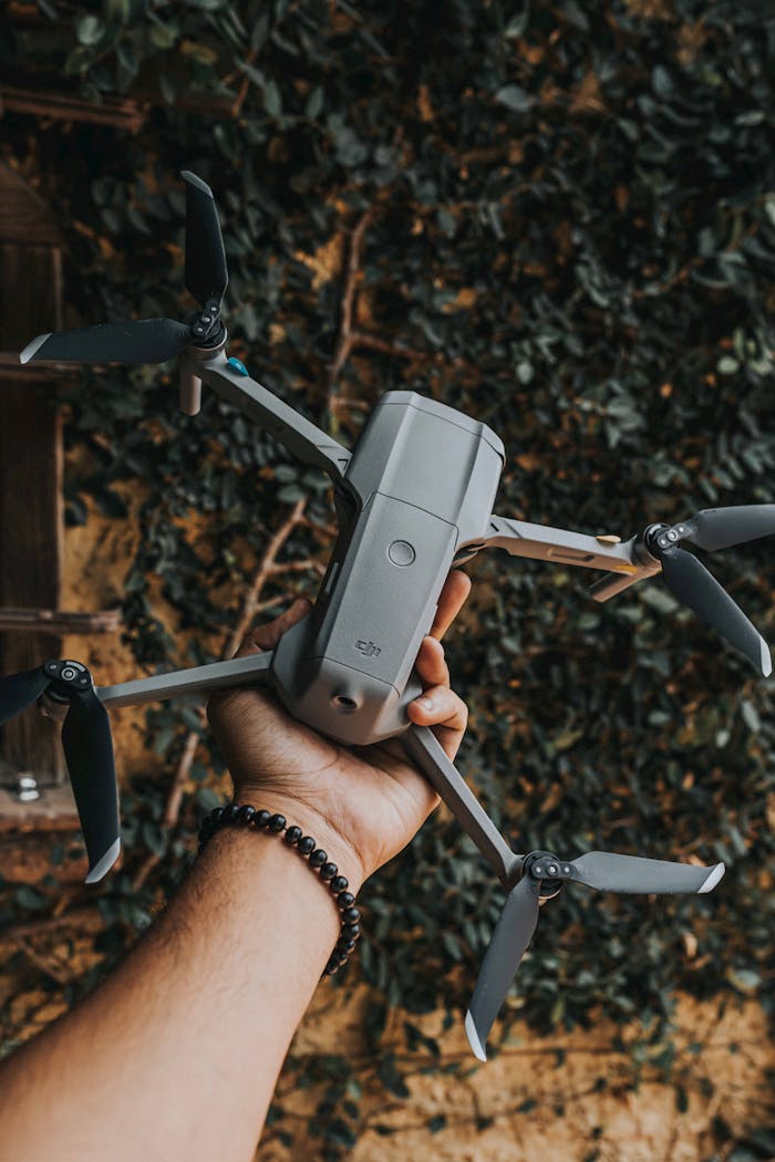 services-04 Close-up of a hand holding a DJI drone, set against a leafy backdrop outdoors.